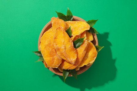 Dried mango chips in a bowl on a green backgroundの写真素材