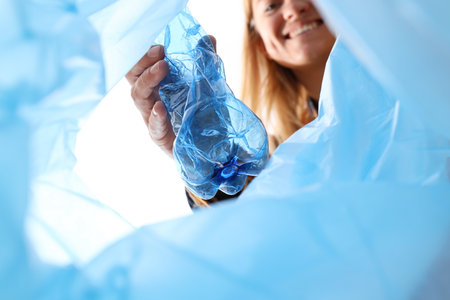 Plastic bottle in female hand and blue garbage bag on white background, close up