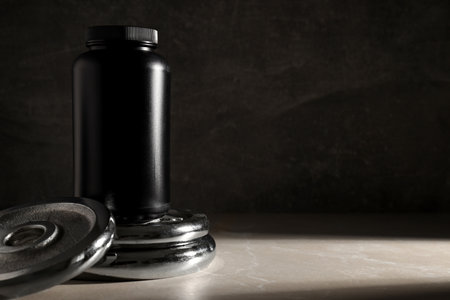 Black plastic jar on metal sport equipment on dark gray background, space for textの写真素材