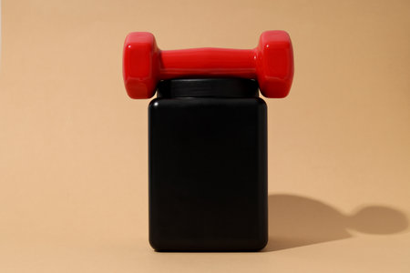 Black plastic jar and red dumbbell on beige backgroundの写真素材