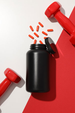 Plastic jar with pills and dumbbells on white and red background, top viewの写真素材