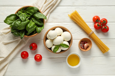 Mozzarella, tomatoes, basil in bowl and spaghetti on wooden background, top viewの写真素材