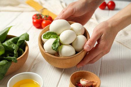 Mozzarella, tomatoes, basil in bowl, hands and spaghetti on wooden background, close upの写真素材