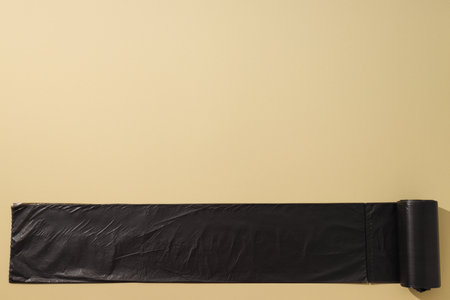Roll of black garbage bags on beige background, space for text
