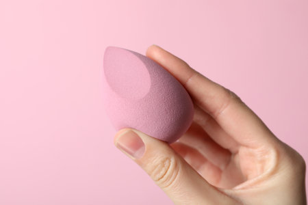 Makeup sponge in hand on pink backgroundの写真素材