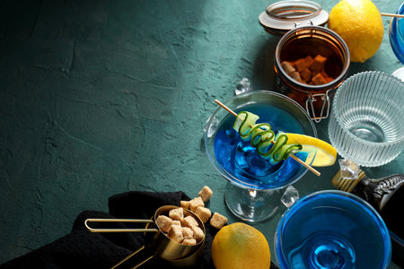 Blue cocktail glasses, lemons, sugar and bottle of alcohol on green background, space for textの写真素材