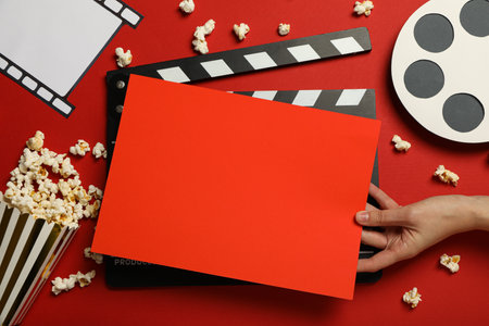 Clapperboard, popcorn, film, reel and hand with red paper on red background, top viewの写真素材