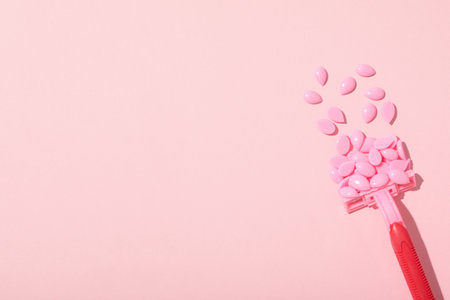 Wax granules for depilation with a razor on a pink background