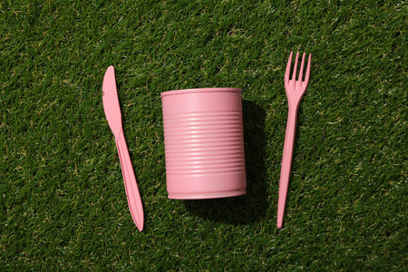 Pink tin can and plastic cutleries on green background, top viewの写真素材