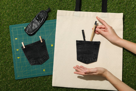 Drawing, cotton bag, denim pockets and hands on green background, top view