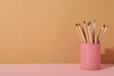 Colored pencils in pink tin can on beige background