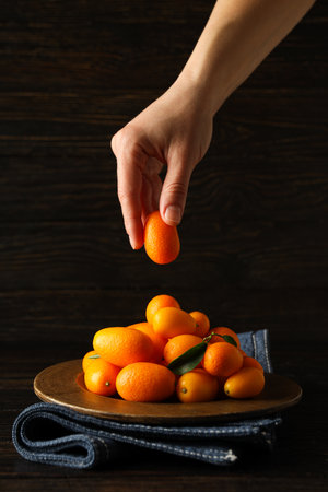 Kumquat on plate, towel and female hand on wooden background