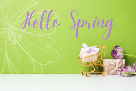 Hello spring, shopping cart, gift boxes and tulips on a green backgroundの写真素材