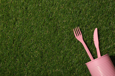 Pink tin can and plastic cutleries on green background, space for textの写真素材