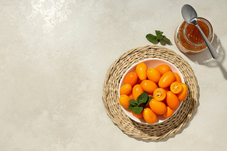 Fresh kumquat fruits in bowl, jar of jam and spoon on light background, space for textの写真素材