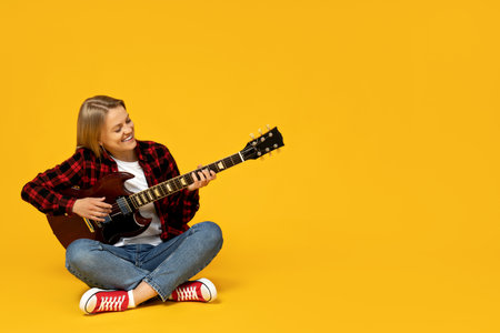 Attractive young girl playing the guitar on a yellow backgroundの写真素材