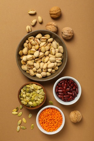 Beans, nuts and seeds in bowls on beige background, top view