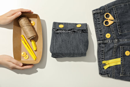 Handmade denim bag, materials, tools and hands on white background, top view