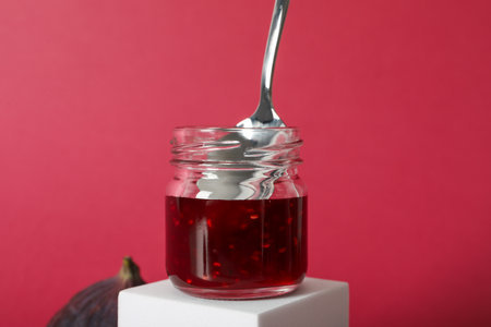 Jar of jam with spoon on white block on pink background, close upの写真素材