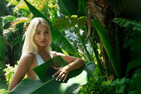 Woman stands in a tropical garden, holding a leafの写真素材