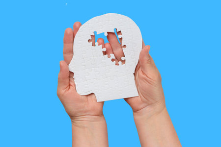 Two hands hold a white human-head puzzle piece with a gapの写真素材