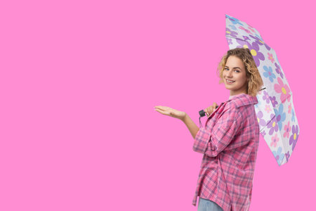 Cheerful young woman with curly hair stands holding an umbrellaの写真素材