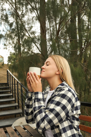 Woman savors warm drink while relaxing outdoors in natureの写真素材
