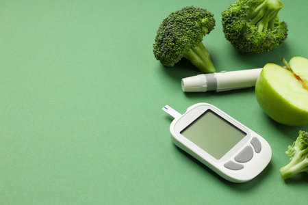 Diabetes testing equipment next to fresh broccoli and green apple