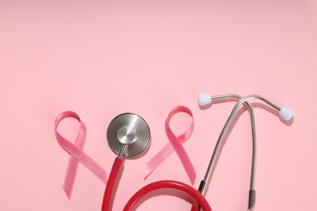 Stethoscope placed beside pink ribbons on pink backgroundの写真素材