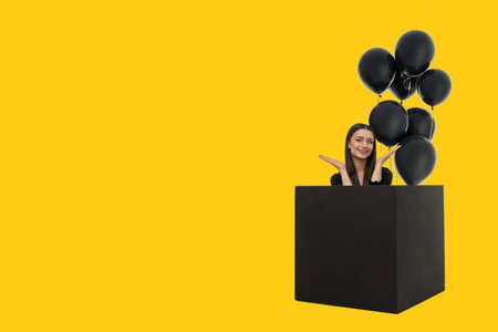 Cheerful woman with long hair in a black box with balloonsの写真素材