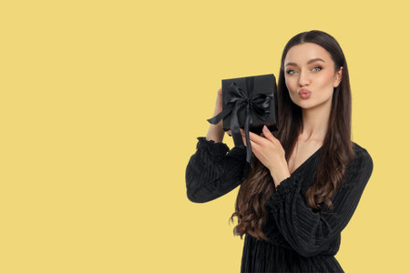 Woman poses with black gift box on yellow backgroundの写真素材
