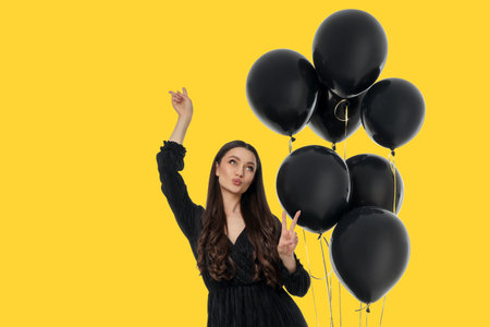 Young woman wearing a black dress poses with black balloonsの写真素材
