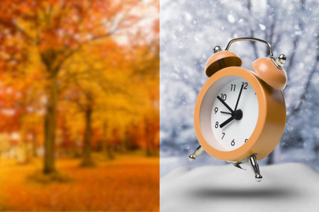 A clock stands tall before autumn trees and snowの写真素材