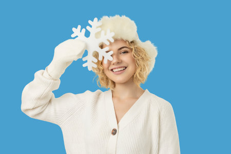 Woman in fluffy white hat holds snowflake on blue bgの写真素材