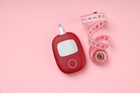 Blood glucose meter next to a measuring tape on pink surfaceの写真素材