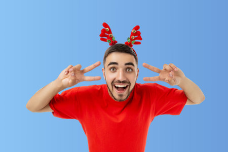 Man wearing red shirt and reindeer antlers poses cheerfullyの写真素材