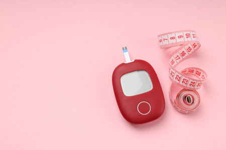 Blood glucose monitor besides measuring tape on pink backgroundの写真素材