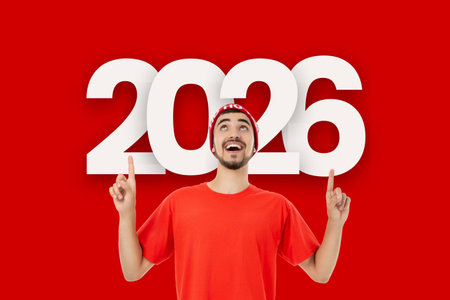 Man in red shirt and Santa hat smiles by 2026 sign