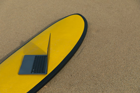 Laptop placed on surfboard on sandy beach under clear sky