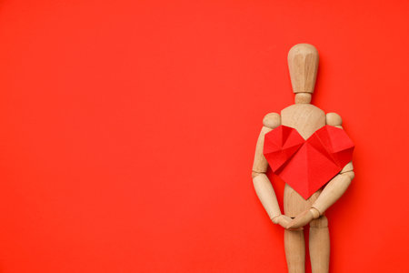 Wooden mannequin stands holding a red heart made of paperの写真素材
