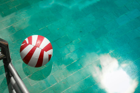 A beach ball floats on clear water near a poolside