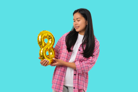 A young woman holds a gold number 8 while smilingの写真素材