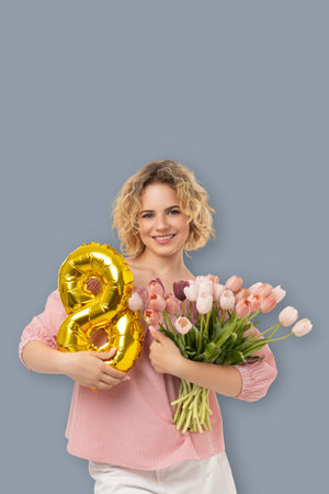 A woman holds flowers and a balloon shaped like a number