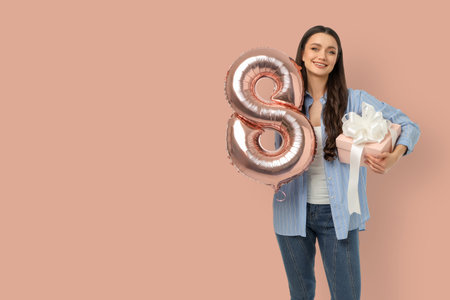 Young woman holds 8 balloon and gift while smiling