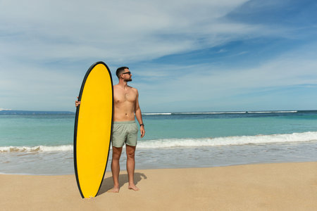 Surfer stands confidently on sandy beach holding a yellow surfboardの写真素材