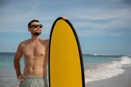 Man stands by the ocean with a surfboard on a sunny day