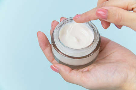 Health and beauty theme female hand holding a glass jar with white body care cream on backgroundの写真素材