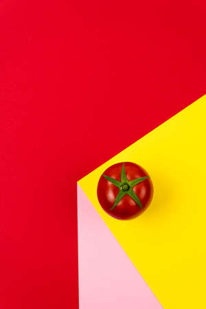 One bright red tomato on colored backgrounds. Illusion of volume. Top view from copy space