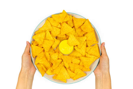 Full plate of tortilla corn chips with cheese sauce in female hands on a white plate. Top view.の写真素材
