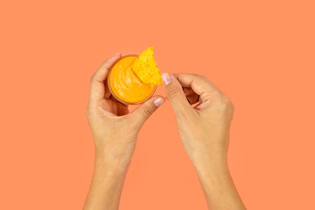 Woman's hands are holding cheese sauce with crispy nachos in a color photo.の写真素材
